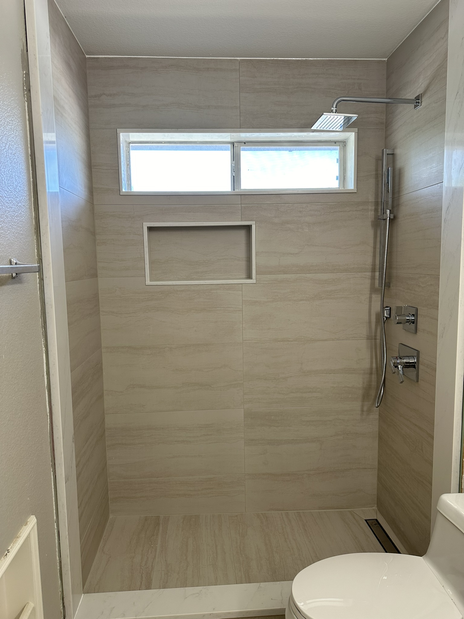 Beige large format tile shower with rainfall head and niche