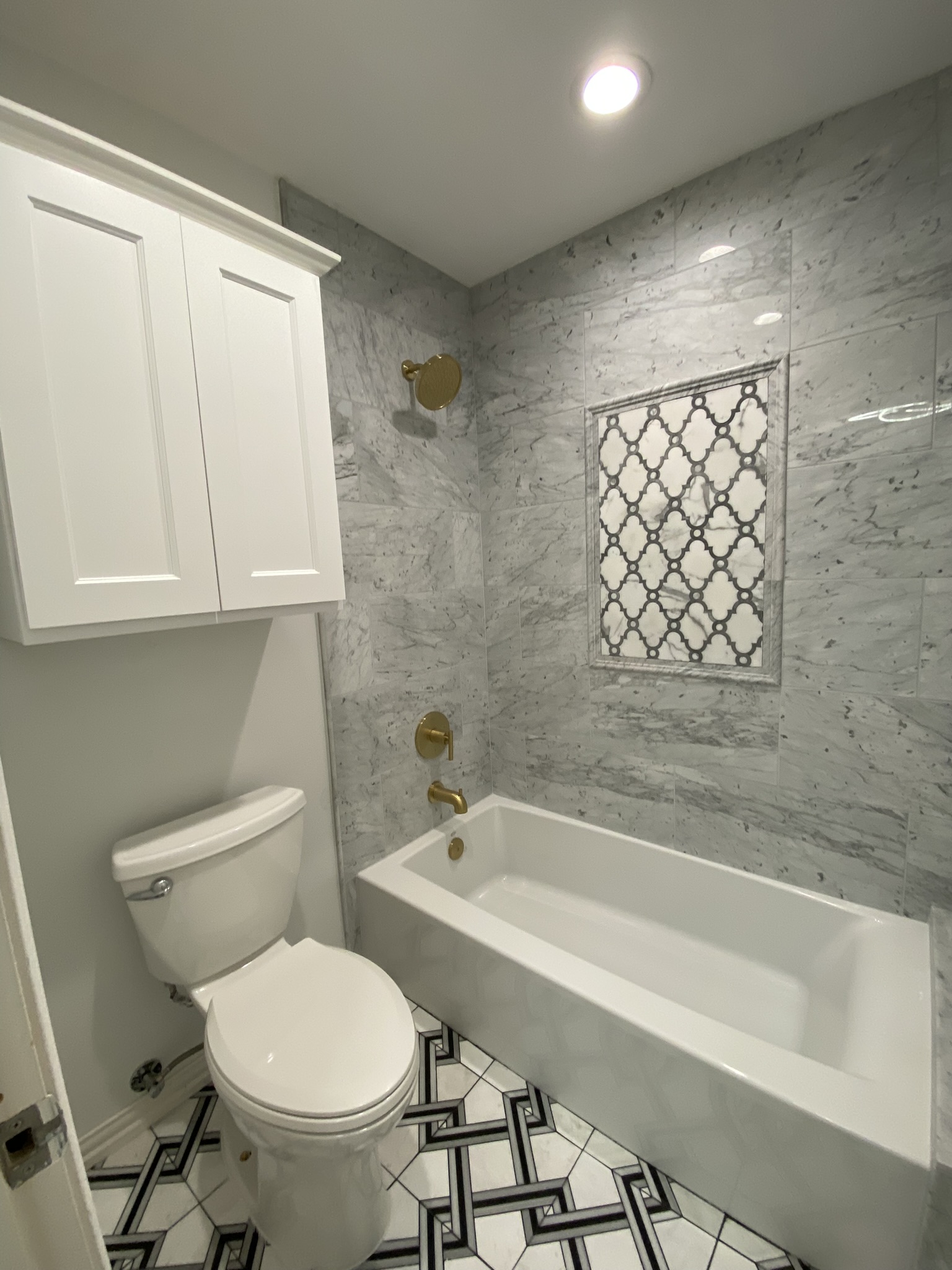 Marble tile bathroom with gold fixtures and geometric floor